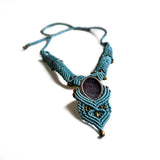 Ayana Crystals blue macrame necklace featuring a central raw amethyst gemstone with intricate knotting and brass beads.